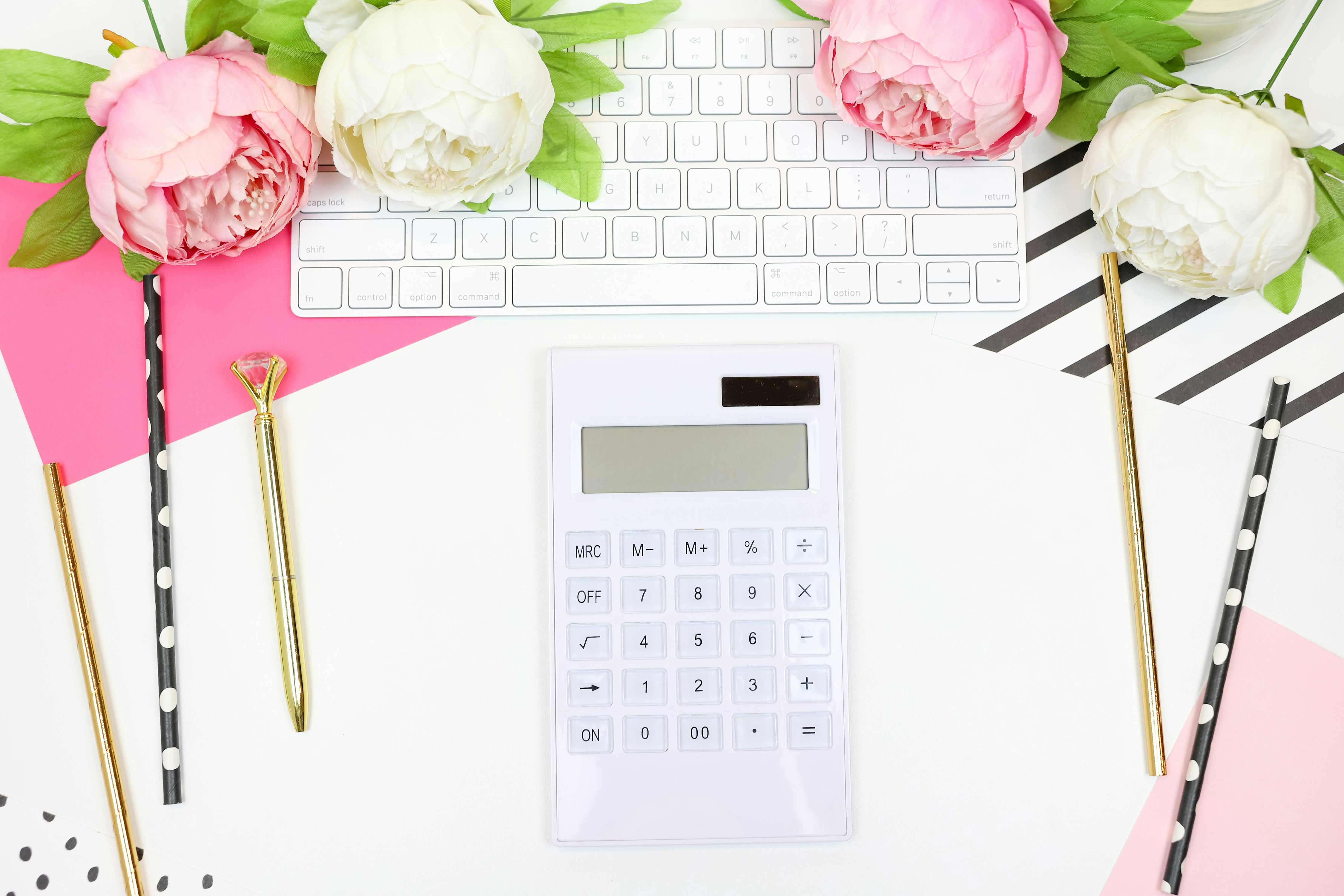 This feminine styled stock photo perfect for lady bosses features hot pink and black props with a white desk, a keyboard, pink and black notecards, pens, a calculator, and more.